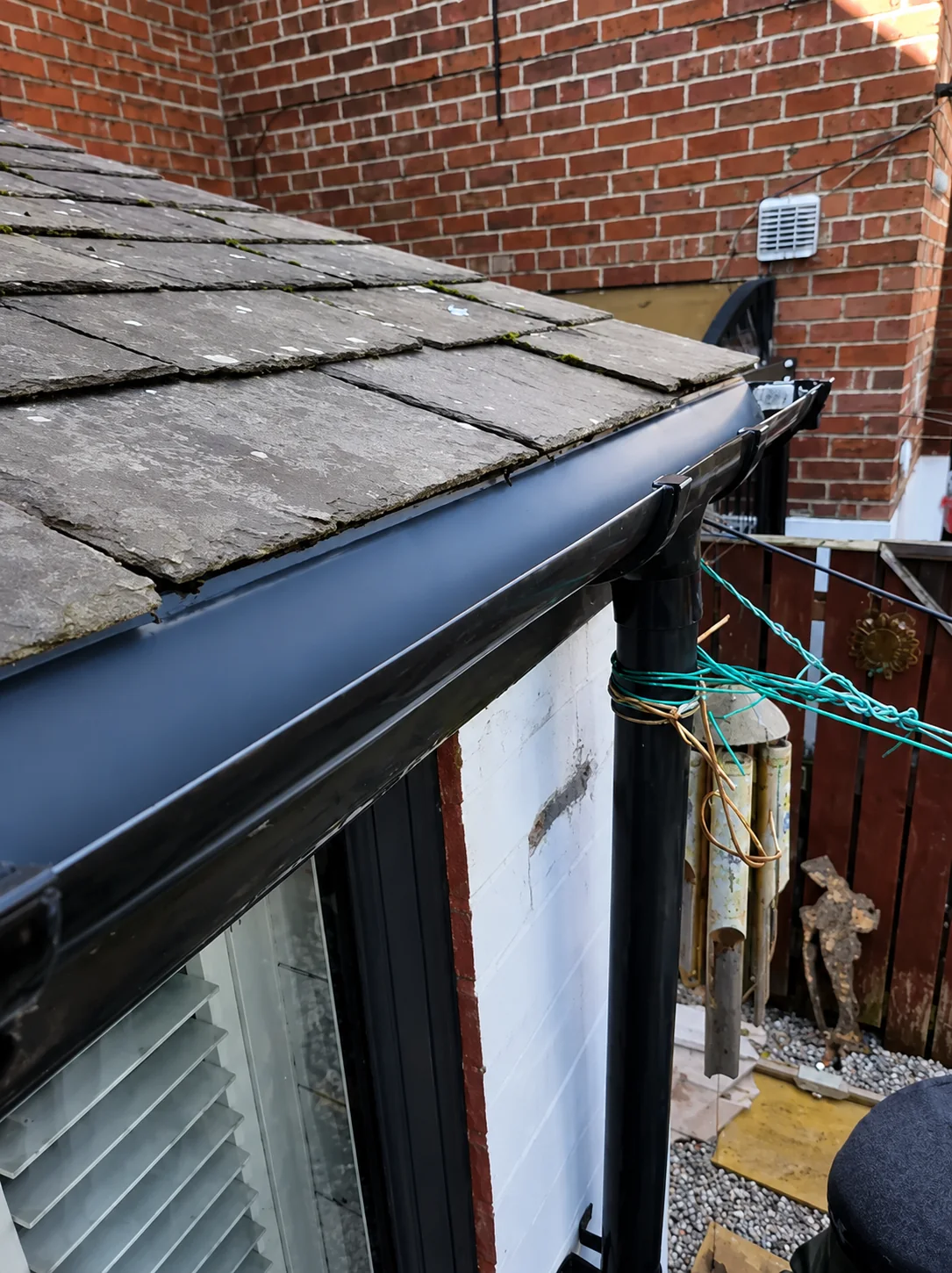 Black guttering and downpipe fitted beneath a slate roof